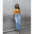 Modelo vestindo calça mom com recortes em jeans claros, combinada com blusa laranja e tênis preto.