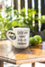 Caneca branca personalizada com alça em forma de coração com a frase "Existe uma chance disso ser caipirinha" ao lado de limões em uma mesa de madeira