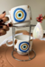 Conjunto de 2 canecas empilháveis brancas com desenho de Olho Grego em azul, amarelo e preto, suportadas por estrutura metálica prateada