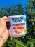Caneca personalizada branca com escrita "Lua em ranço, ascendente em tretas" em letras pretas e desenhos coloridos, sendo segurada por uma mão com tatuagem, ao ar livre com céu azul e árvores ao fundo.